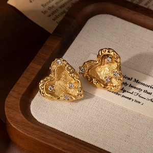 Golden heart earrings with lava texture and crystals displayed on a wooden tray