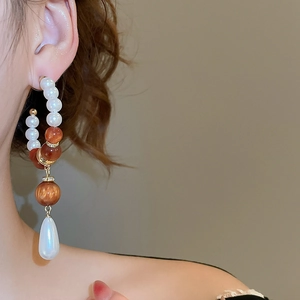 Detail of drop earrings with white pearls and amber resin beads on a golden metal chain