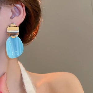 Detail view of irregular blue marble drops on golden wave studs worn on an ear