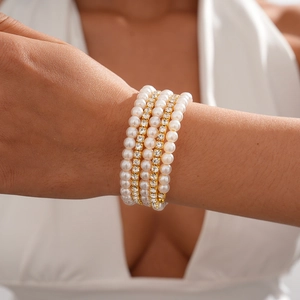 Detail of multilayer gold charm bracelet with white pearls and sparkling diamonds