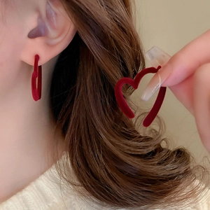 Dettaglio degli orecchini a cuore rosso con trama floccata indossati per un look festivo