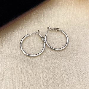 Minimalist silver hoop earrings with polished metal finish on beige textured background