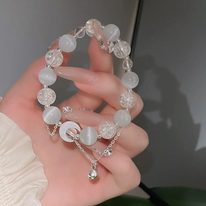 Detailansicht eines Katzenauge-Perlenarmbands mit silbernem Mondanhänger und Glocke