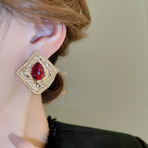 Close-up of vintage gold earring featuring a large red teardrop gemstone on a model