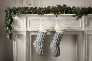 Detail of two grey cable knit Christmas stockings hanging on a white festive mantel
