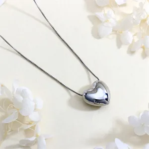 Detailed view of a silver heart-shaped pendant with a polished box chain on a textured surface