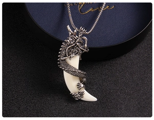 Close-up of a silver dragon pendant with white tooth charm on a black textured background