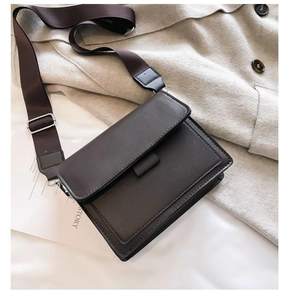 Detail of a dark brown crossbody bag with a wide nylon strap and silver metal buckle