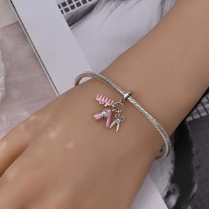 Close-up of silver snake chain bracelet with pink enamel comb and hairdryer charms