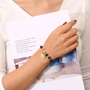 Dettaglio di un bracciale di perline nere con ciondolo a cuore LOVE dorato sul polso di una modella