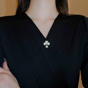 Close-up of a gold-plated flower brooch with clover petals and a zircon heart on black fabric