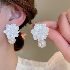 Detail showing white resin flower earrings with round pearl pendant on a model