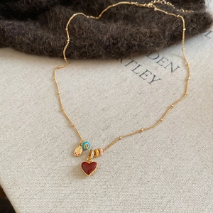 Detail of 18k gold plated heart necklace with red enamel and lucky charm pendant