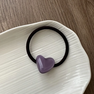 Detail of purple acrylic heart charm on a black high-elastic hair tie on a white plate