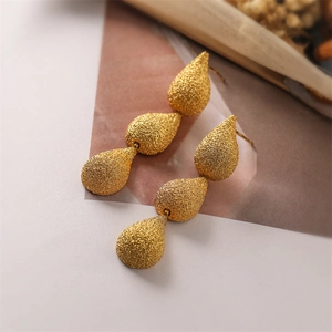 Macro shot of gold teardrop earrings with matte texture and modern geometric three-tier design
