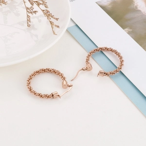 Détail de boucles d'oreilles créoles or rose avec texture tressée sur porcelaine blanche