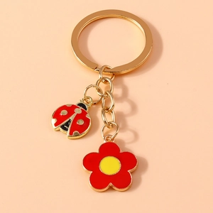 Macro view of metal ladybug and flower charms on a golden keychain with pink background