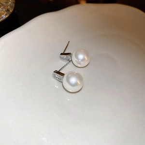 Macro detail of pearl earrings with rectangular cubic zirconia in a white ceramic dish