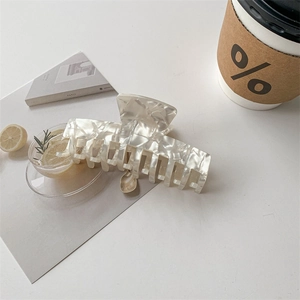 Detailed view of a white pearlescent acetate hair claw clip on a minimalist desk