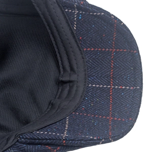 Detail of tweed newsboy cap showing blue herringbone fabric with red plaid pattern