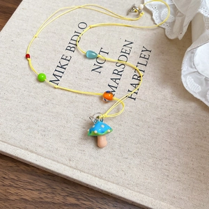 Vue détaillée du pendentif champignon bleu sur un cordon tressé jaune avec perles