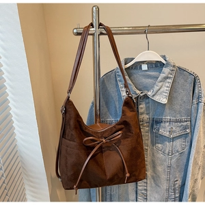 Brown suede shoulder bag with bow detail hanging against a denim jacket backdrop