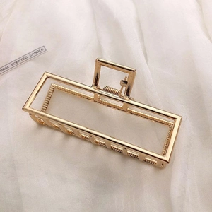 Detail of a large gold metal hair claw clip with rectangular hollow design on satin fabric