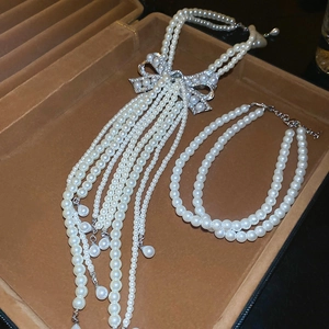 Détail du collier de perles avec nœud en cristal et pompon dans un écrin en velours