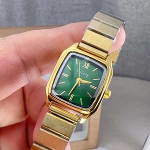 Detail of a square green dial watch with a golden metal stretch strap on a wrist