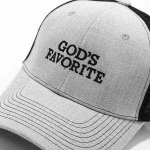 Detailed close-up of 'GOD'S FAVORITE' embroidery on gray mesh trucker baseball cap