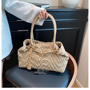 Detail of beige bouclé handbag with leather handles and decorative long charms on a chair
