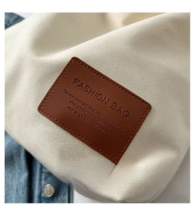 Close-up of canvas tote bag showing the brown leather patch with embossed lettering