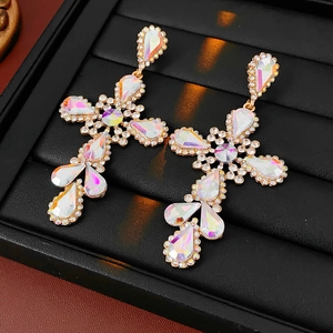 Macro shot of gold cross earrings with iridescent rhinestones on a black velvet tray