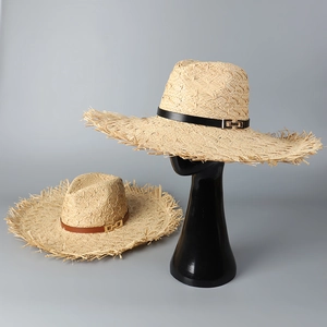 Detail of wide brim raffia hats featuring frayed edges and decorative metal buckle straps