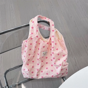 Close-up of pink canvas tote bag featuring red heart patterns and brand label