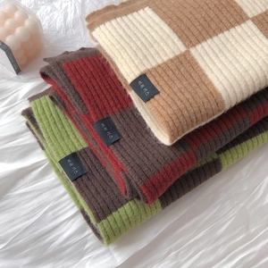 Close-up of stacked checkerboard knit scarves in brown, red, and green ribbed wool