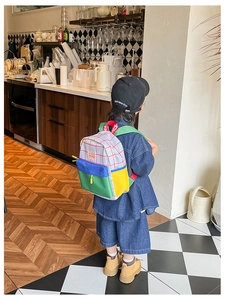 Rear view of a child wearing a colorful patchwork canvas backpack with white grid pattern