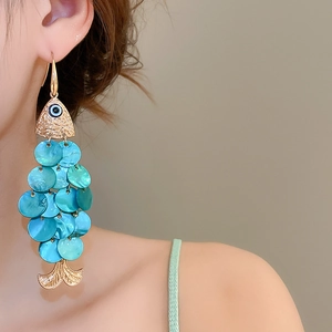 Detailed close-up of golden fish-shaped earrings featuring blue-green shell pendants