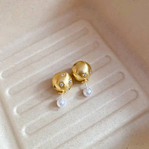 Macro detail of gold-beaded earrings with inlaid zircons and pearls on a beige tray