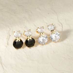 Elegant gold bow stud earrings with black and clear cubic zirconia on stone background
