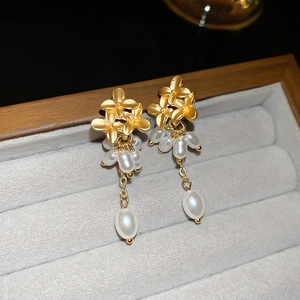 Detail of gold flower earrings with hanging pearls displayed in a premium velvet box