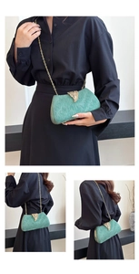 Detail of green silk clutch bag featuring a gold leaf clasp and metal chain strap