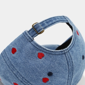 Détail macro de la casquette en jean avec broderie de cœurs et boucle de serrage
