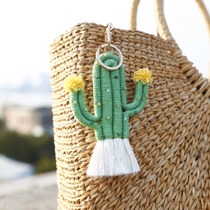 Handmade green cactus keychain with beads, yellow pompoms and white tassel on a straw bag