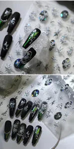 Détail macro des stickers à ongles floraux argentés M-534 sur des faux ongles noirs mats