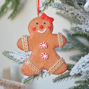 Gingerbread man Christmas tree ornament with red bow on snowy pine branch