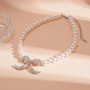 Collana di perle vintage con un ciondolo a fiocco di strass su sfondo beige caldo