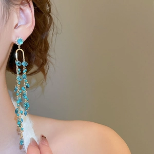 Macro side view of elegant long gold tassel earrings with sea blue crystal stones