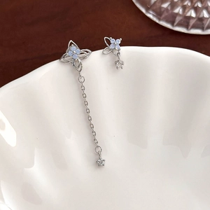 Detail of silver asymmetric flower butterfly earrings with blue crystals on white bowl