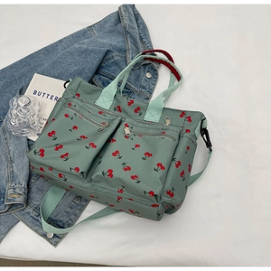 Detail of grey-green tote bag with cherry print and dual front zipper pockets